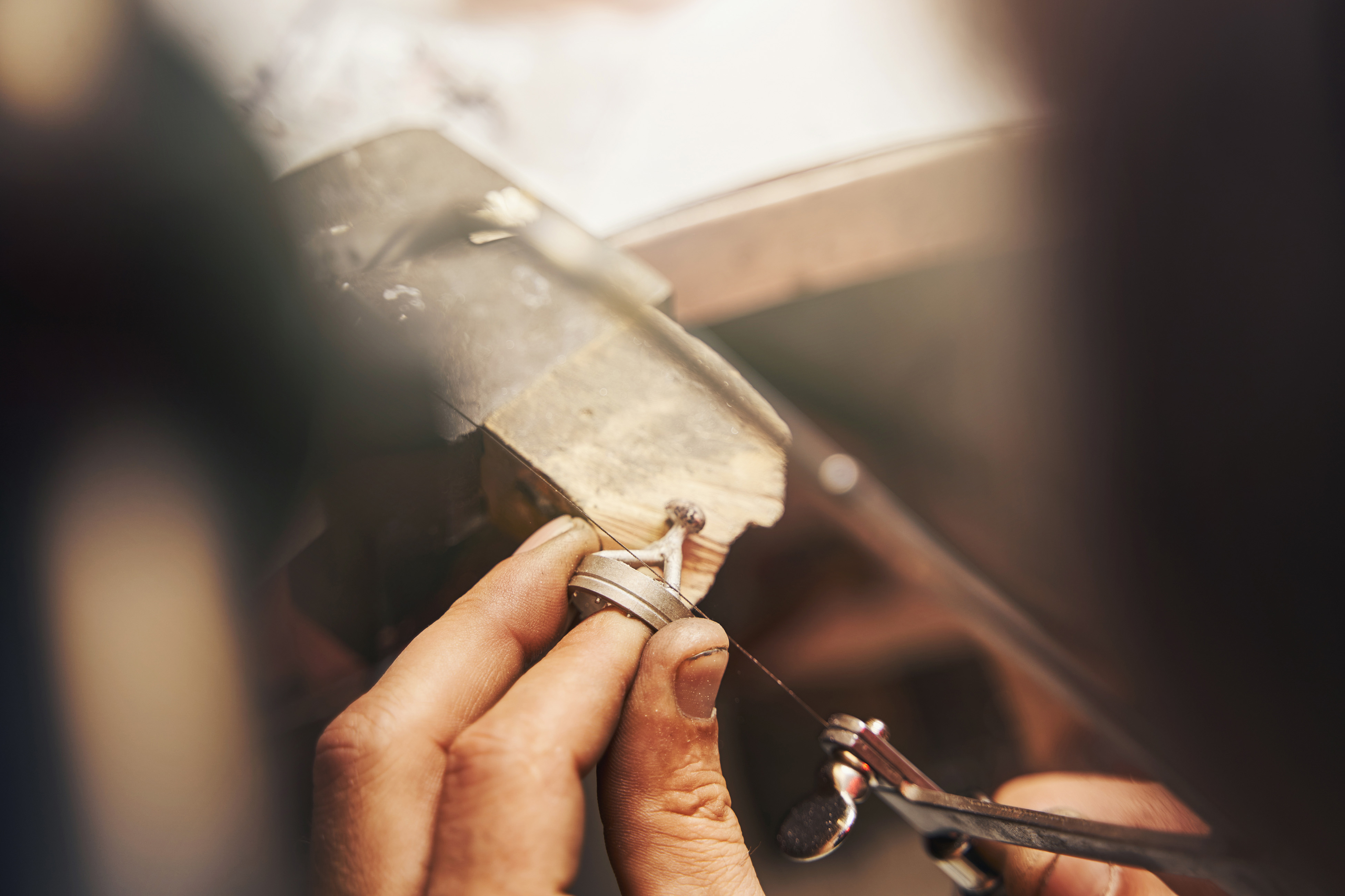A person sawing an unfinished ring at a timber jewellery bench.