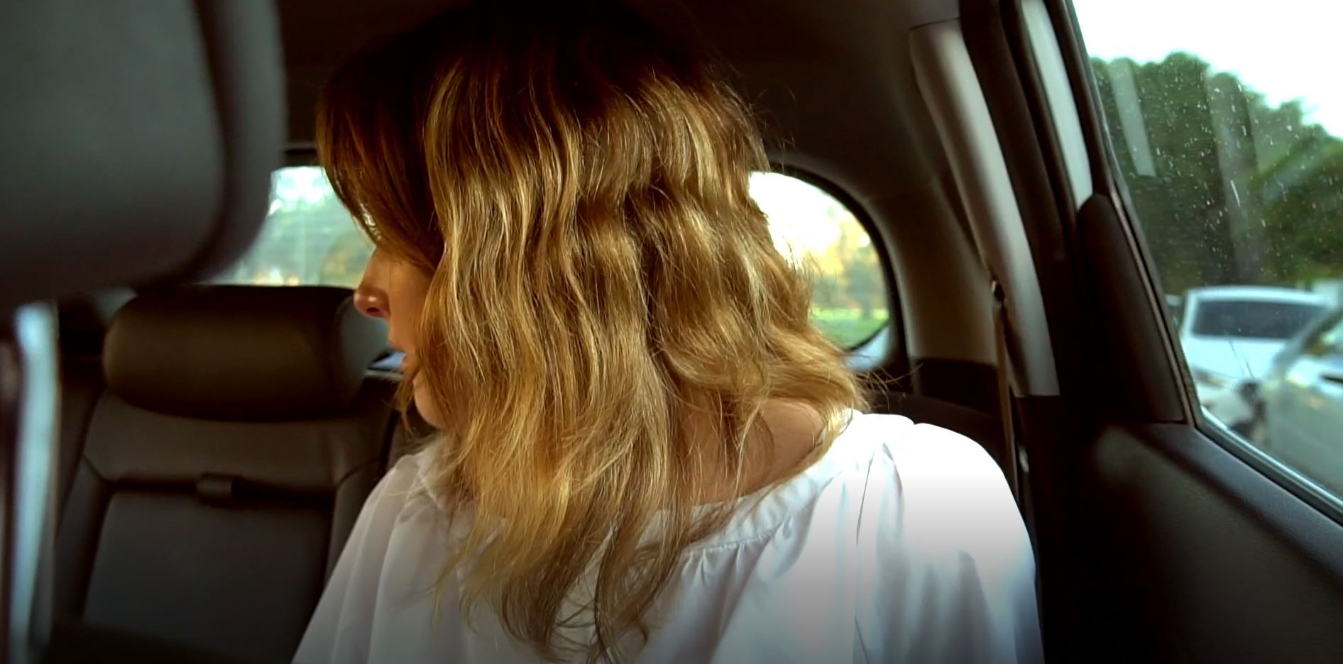 Photograph of the side of a girl's head. She is sitting in a car with grey interior, and she has shoulder length, wavy blonde hair.