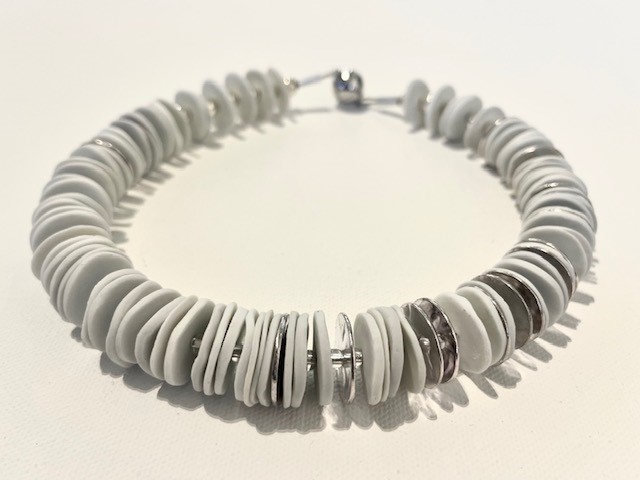 A short necklace of thin white ceramic discs stacked around a rigid loop of silver the piece has a spherical closure mechanism.