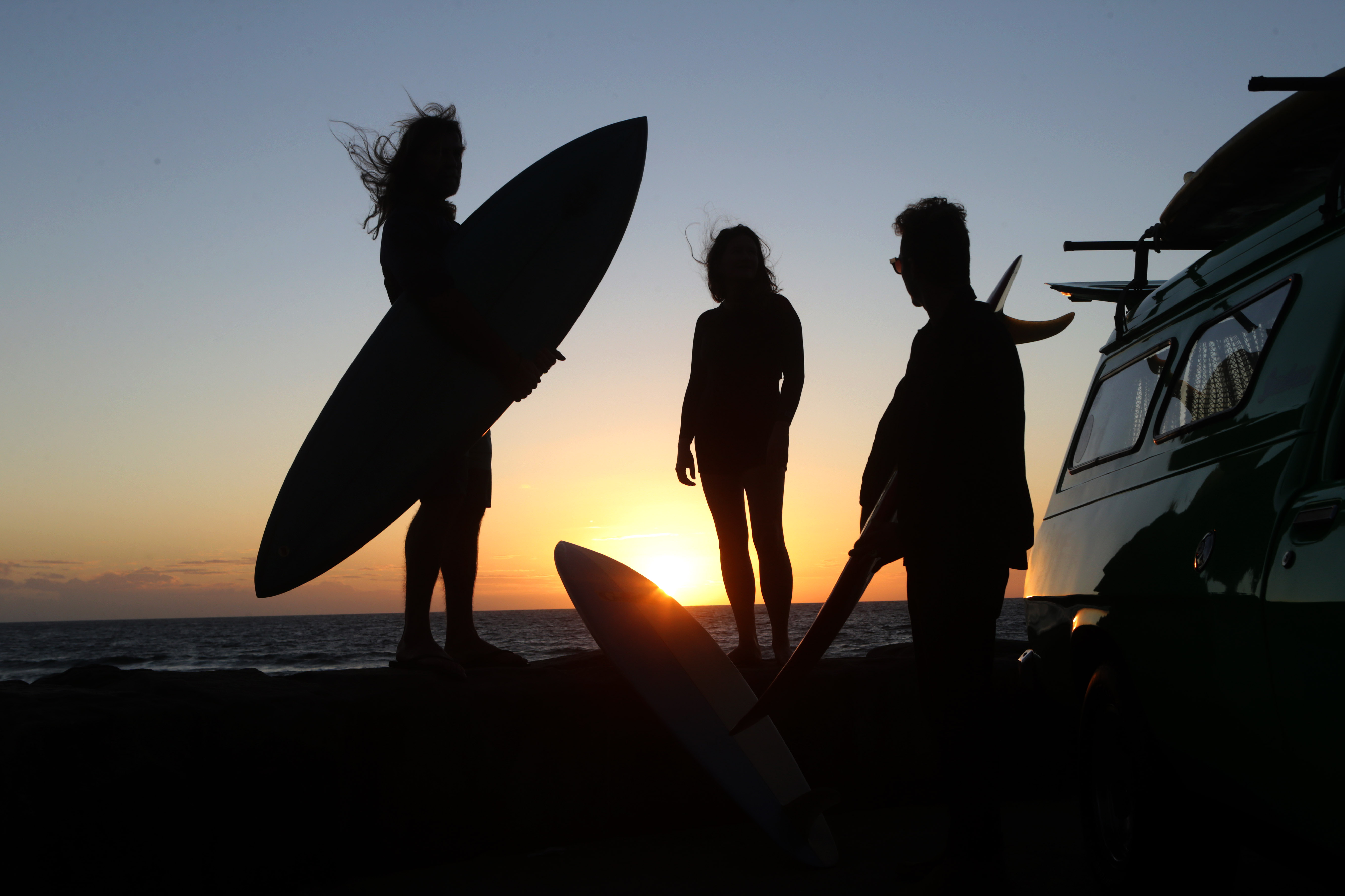 A photograph of three surfers at dawn.