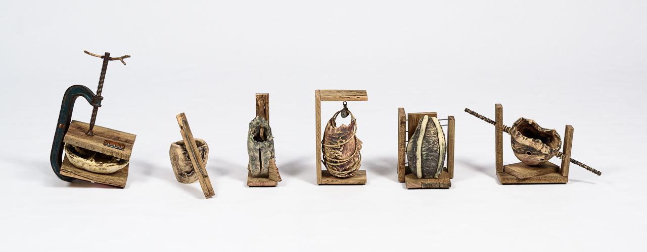 A series of six small ceramics objects bound in structures of metal and timber.