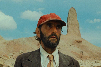 A man in a suit and baseball cap in the desert.