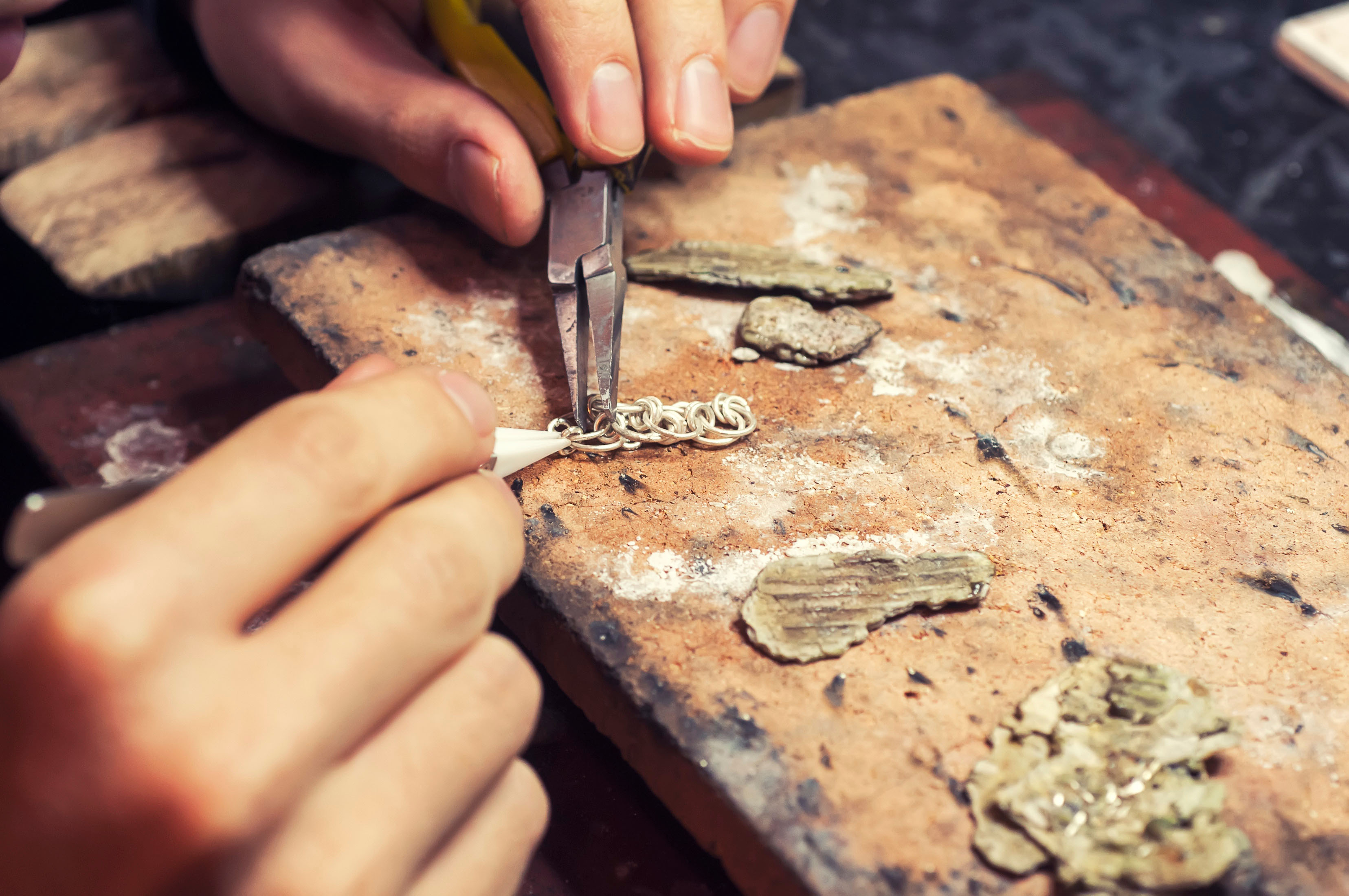 A jeweller's hands making a silver chain at a timber bench.