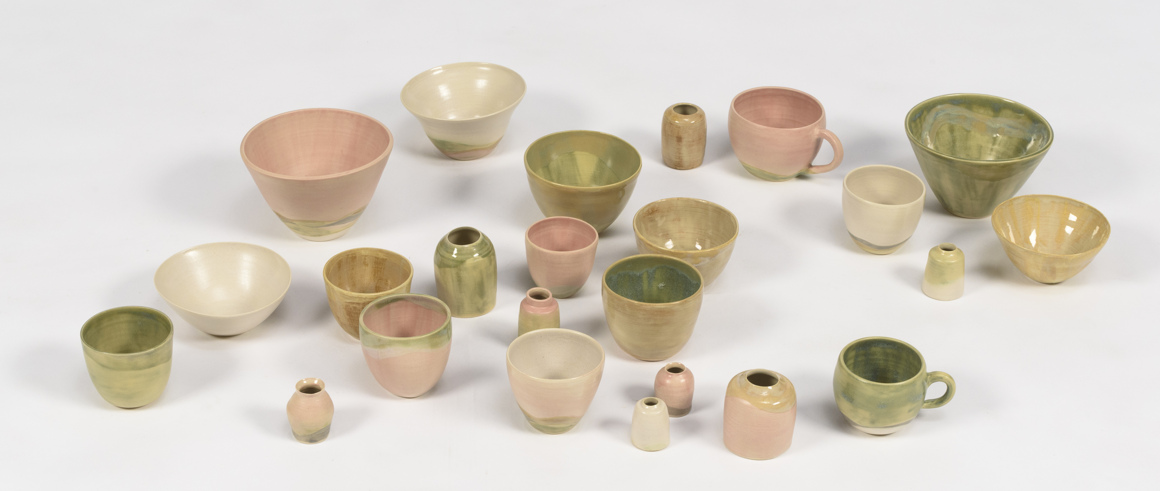 24 ceramic vessels of various shapes and sizes in glazes of shades of pink, green and white.