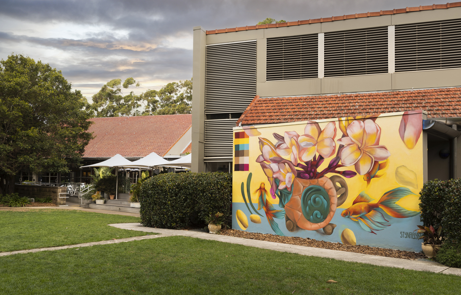 Photograph of a colourful outdoor mural featuring fish, frangipani flowers and a teapot.