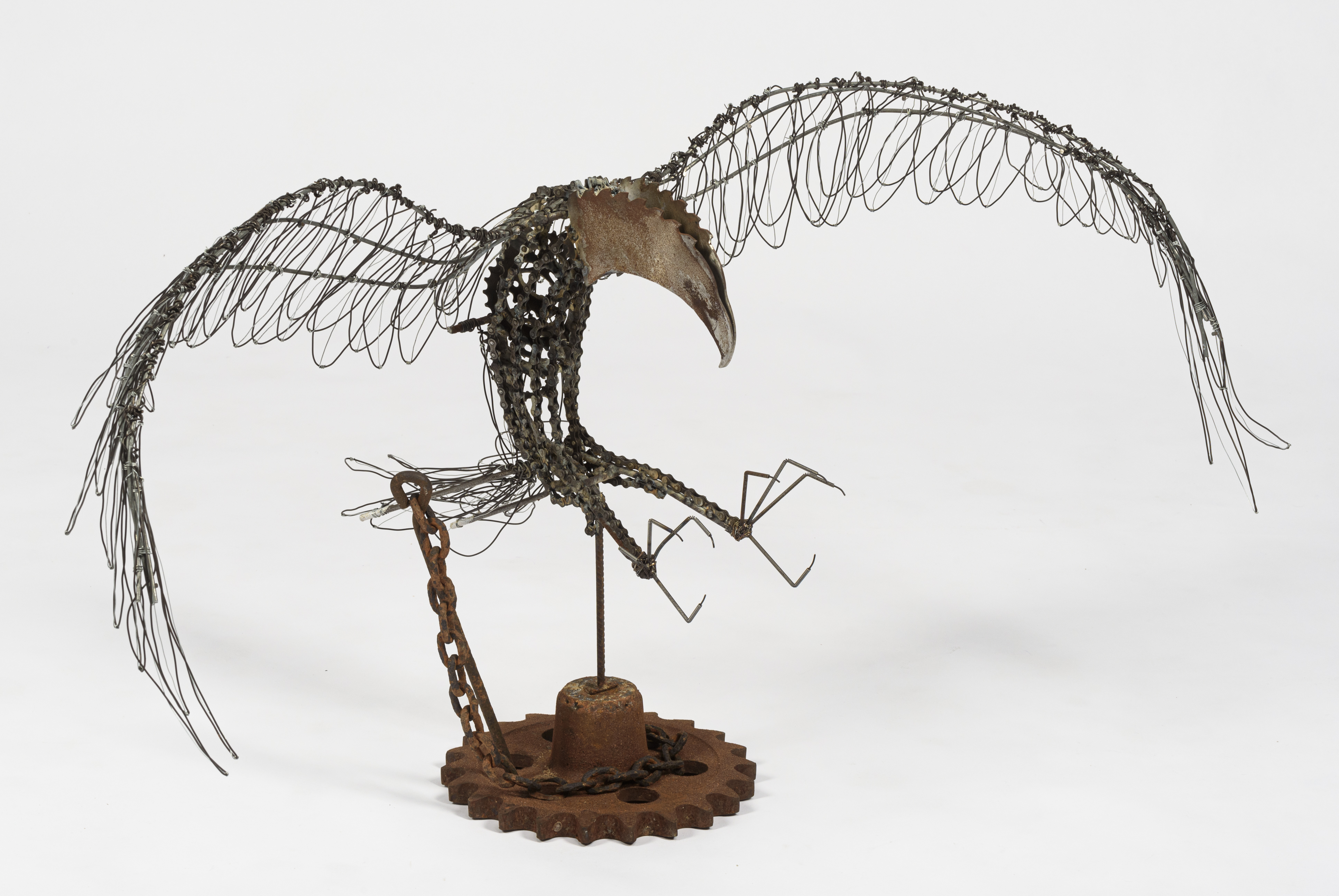 A sculpture of a bird chained to a tether made from recycled wire and metals.