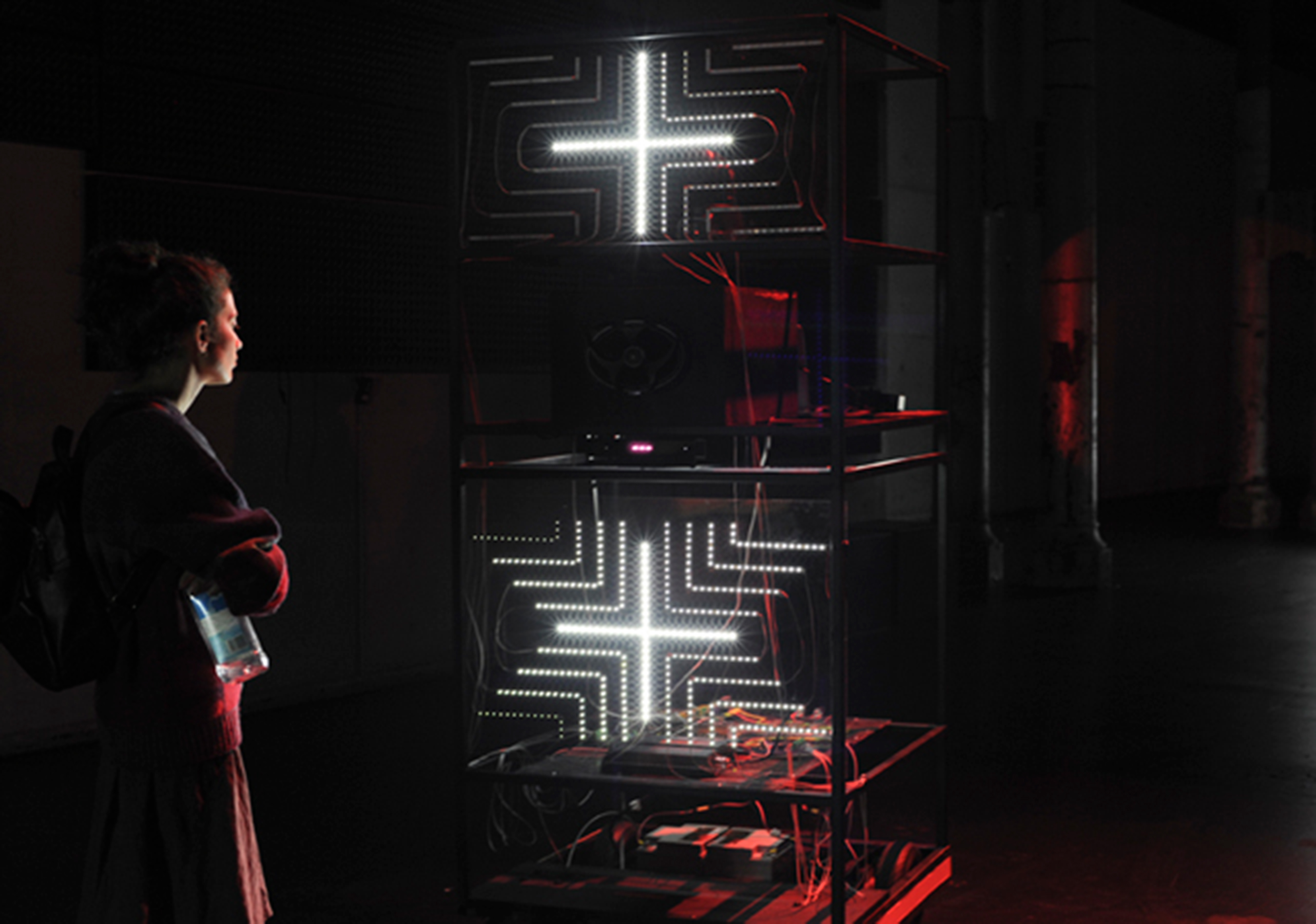 A person in a dark room standing before a large structure that has white illuminated crosses on it,