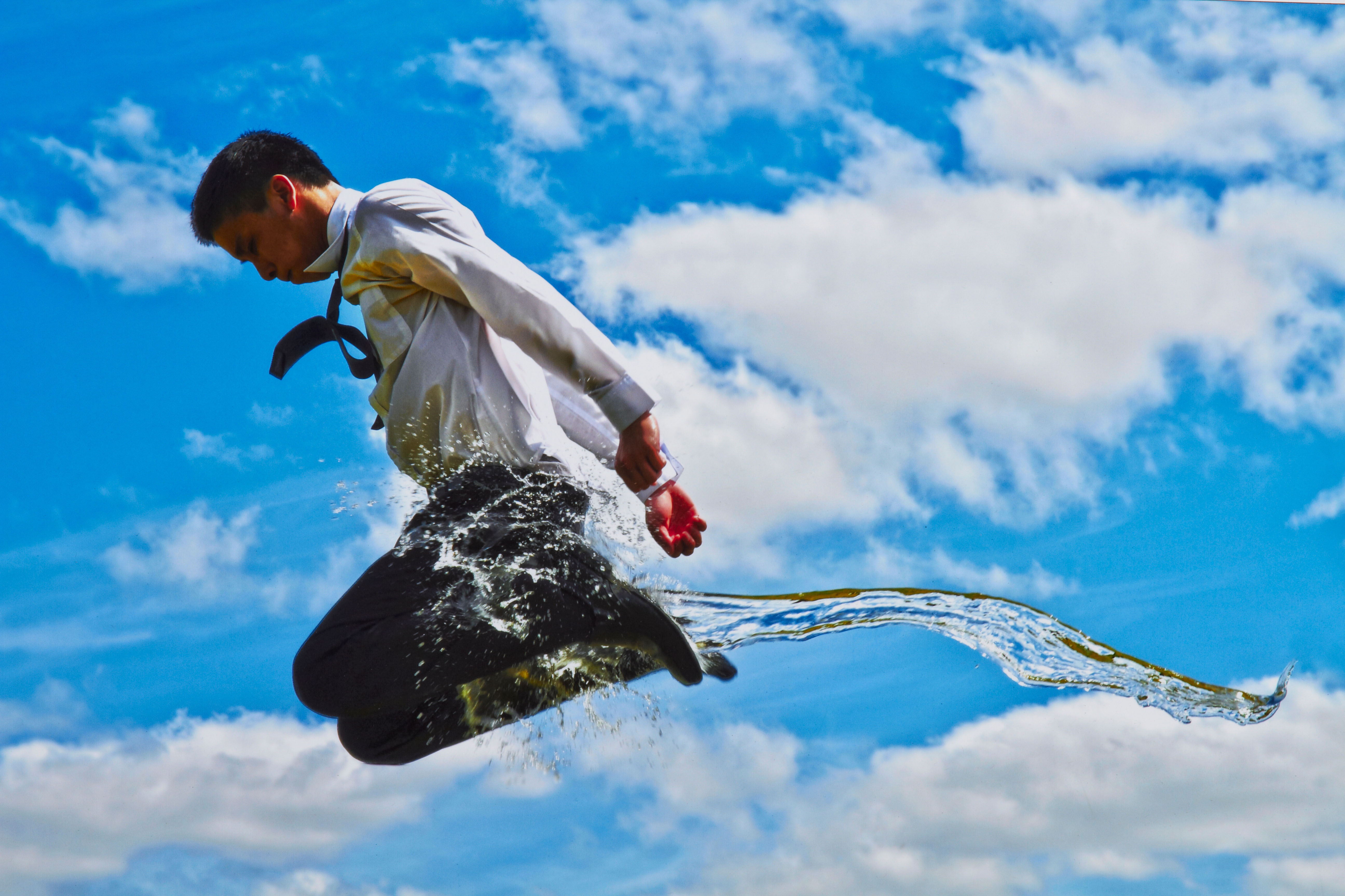 A photomedia work of a male student in a school uniform jumping across the frame with a splash of water going in the opposite direction.