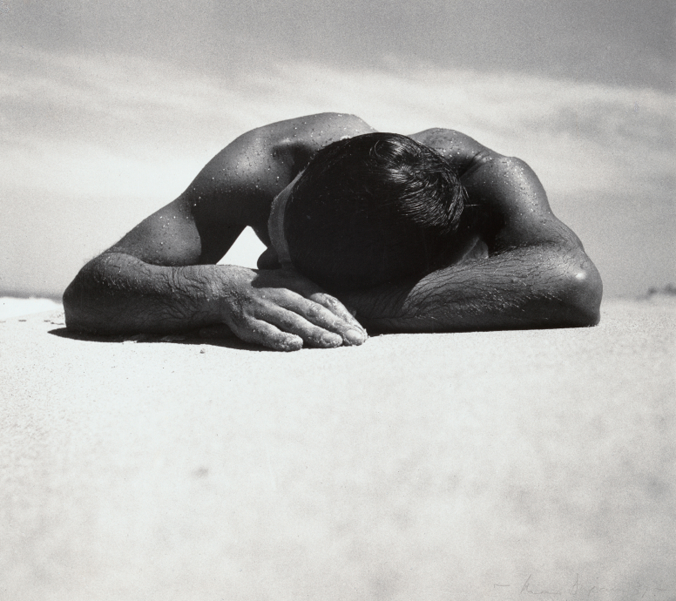 Black and white photograph by Max Dupain of a male sunbather lying face down with their head resting on crossed arms.