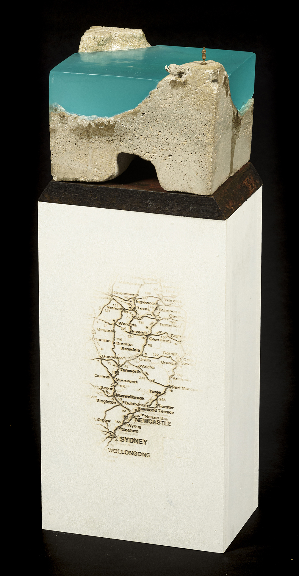 A sculpture of aqua coloured epoxy resin and concrete on a white plinth that has a map applied to its surface.