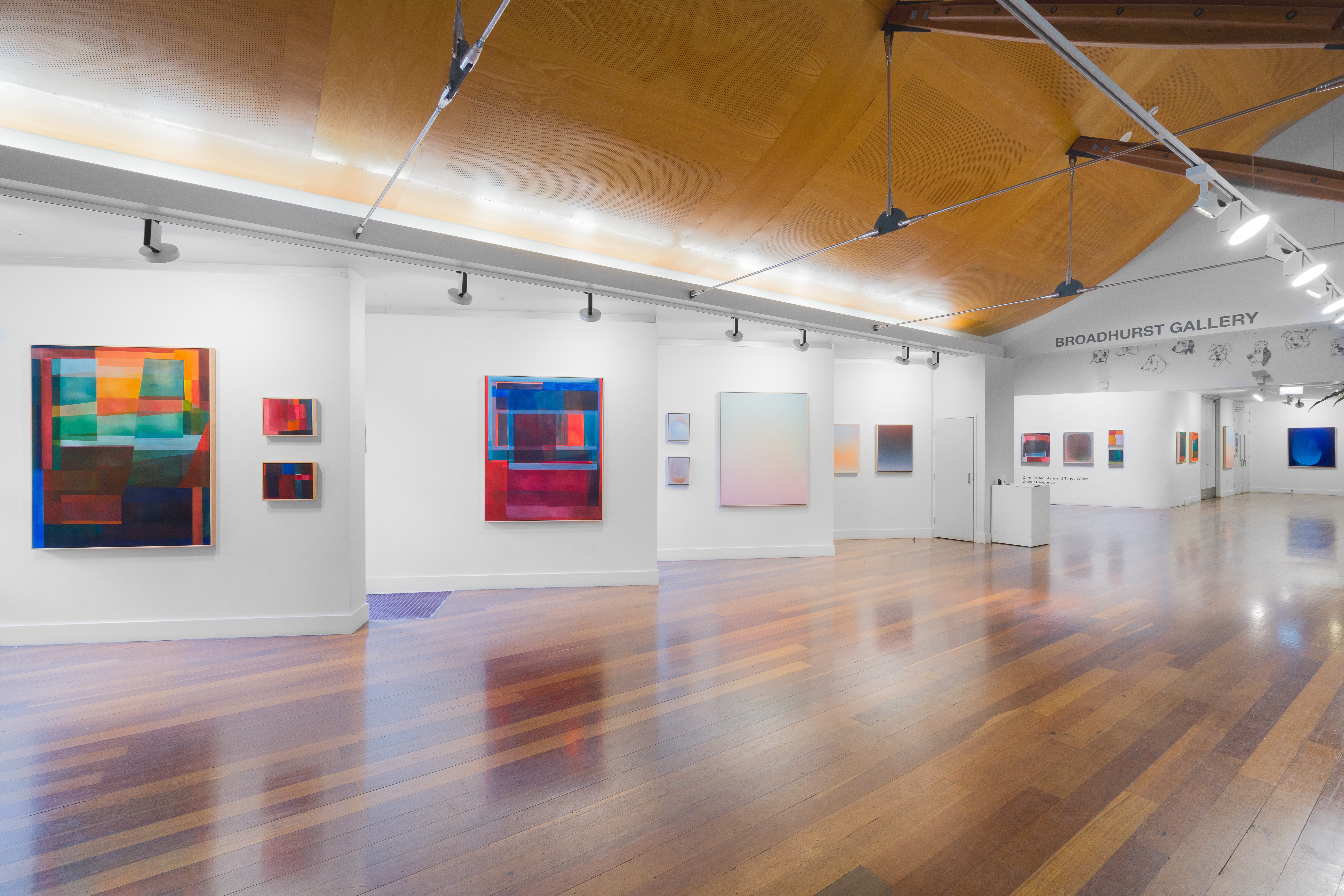 A large gallery space with polished timber flooring. On the walls are several large colour field paintings.