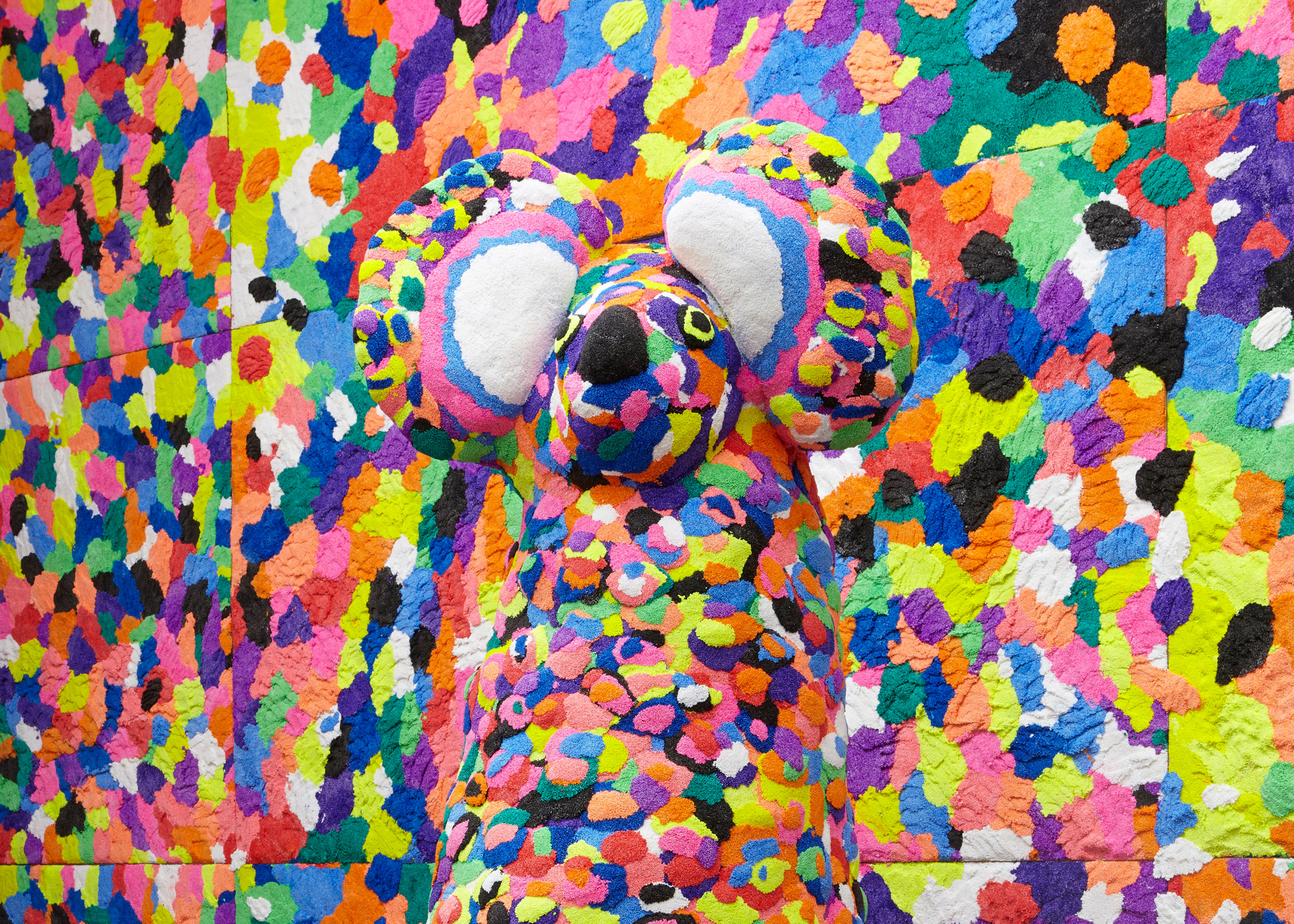 A koala shaped totem covered in foam made up of many different, bright colours. The background is made of the same material.