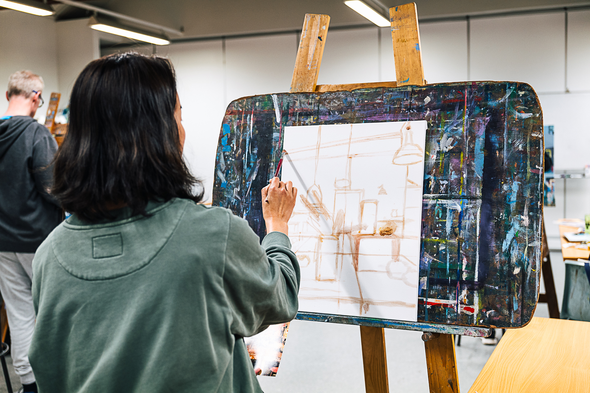 Woman in green shirt standing at easel blocking out her canvas.