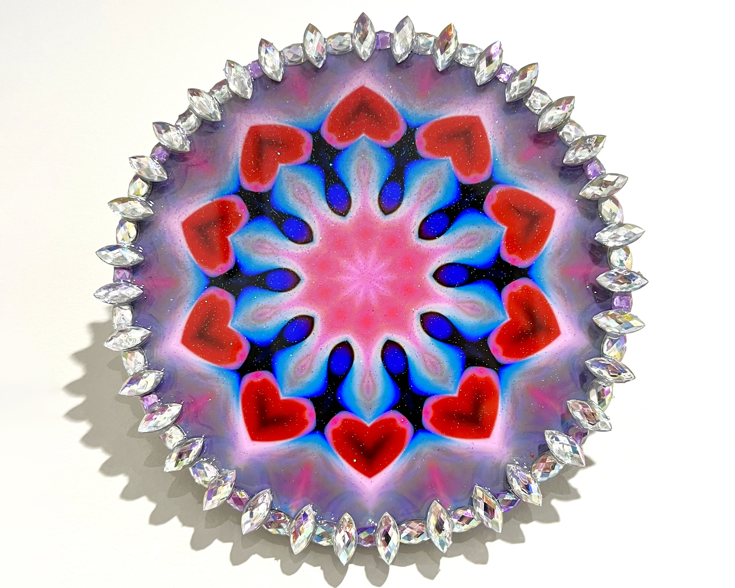 A circular abstract image in reds, blues and purples with a border of clear jewels.
