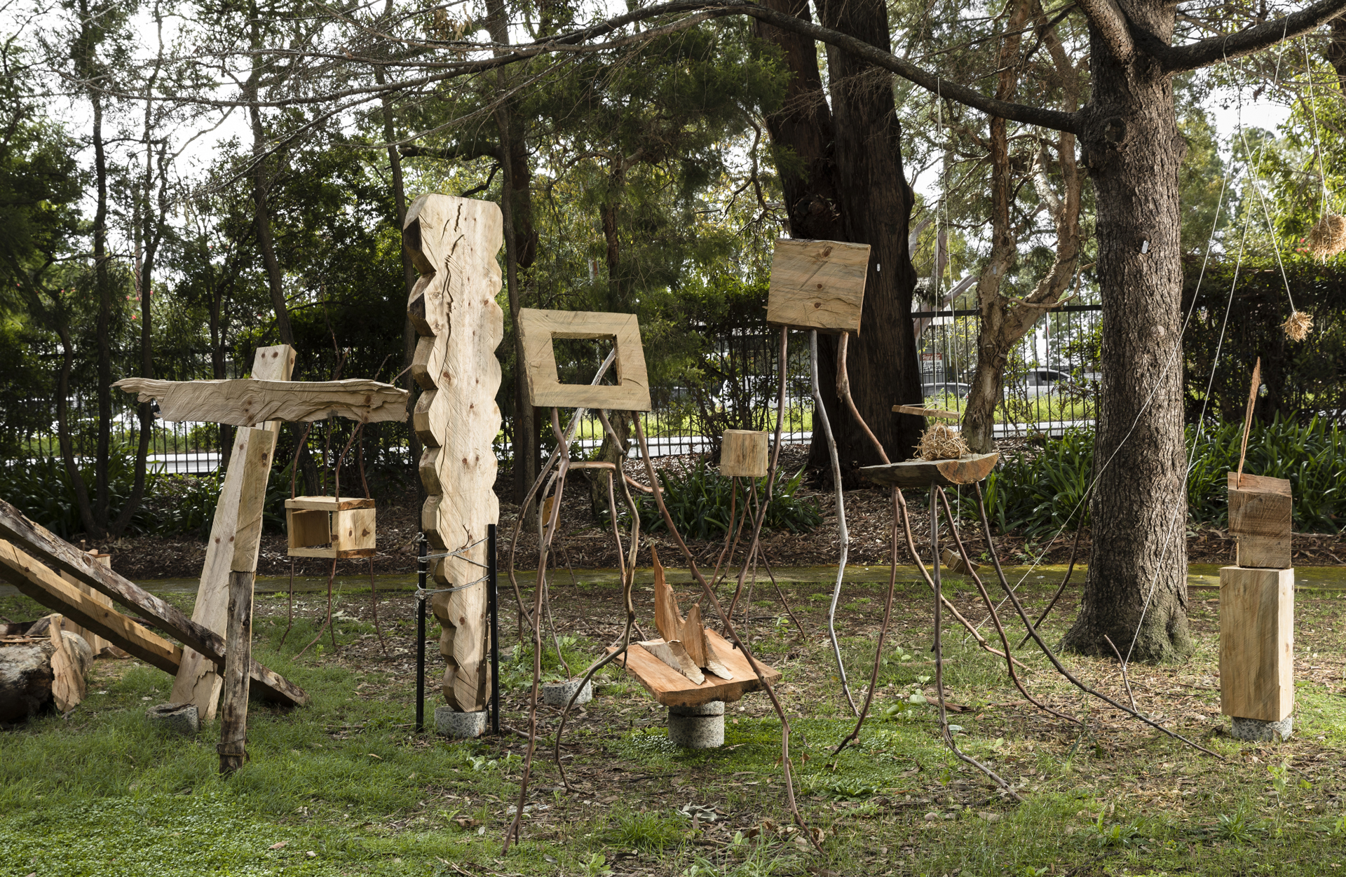 A group of wooden sculptures of varying sizes shapes and styles surrounded by trees.