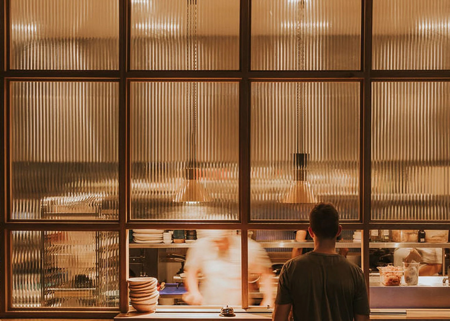 Phtograph of server waiting at kitchen pass that has glass decorative glass panelled screen.