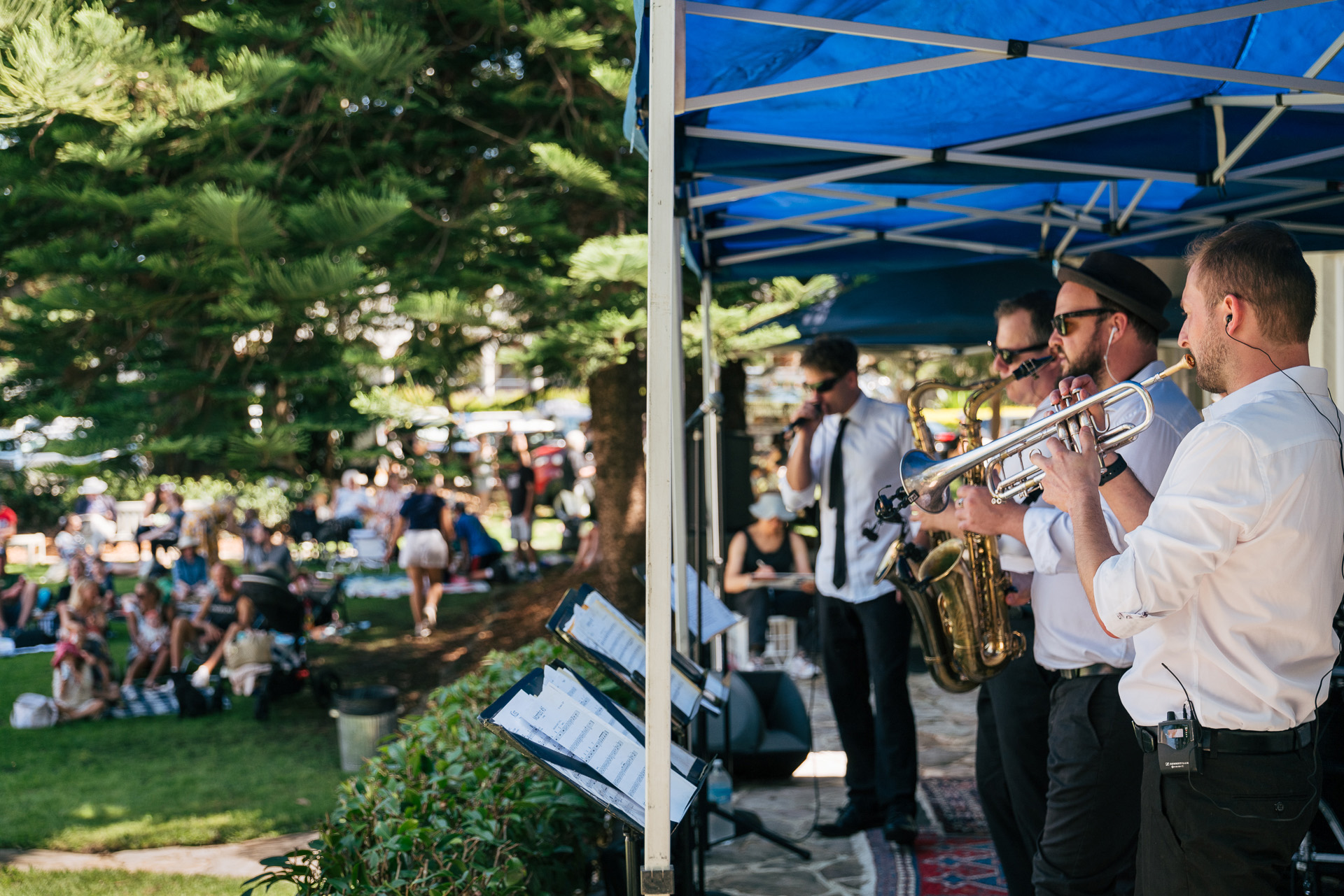 Brass band playing under blue marquee outside on a sunny day.