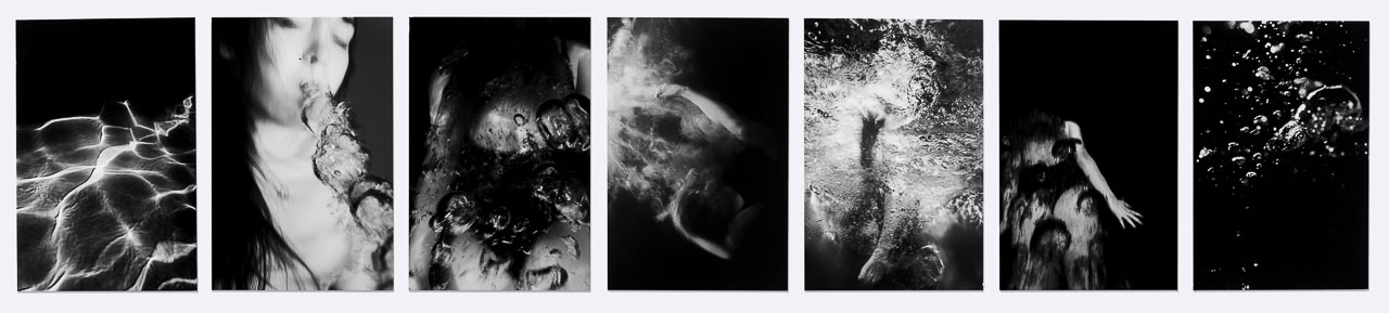 A series of seven black and white underwater photographs of a figure moving under and through the water.