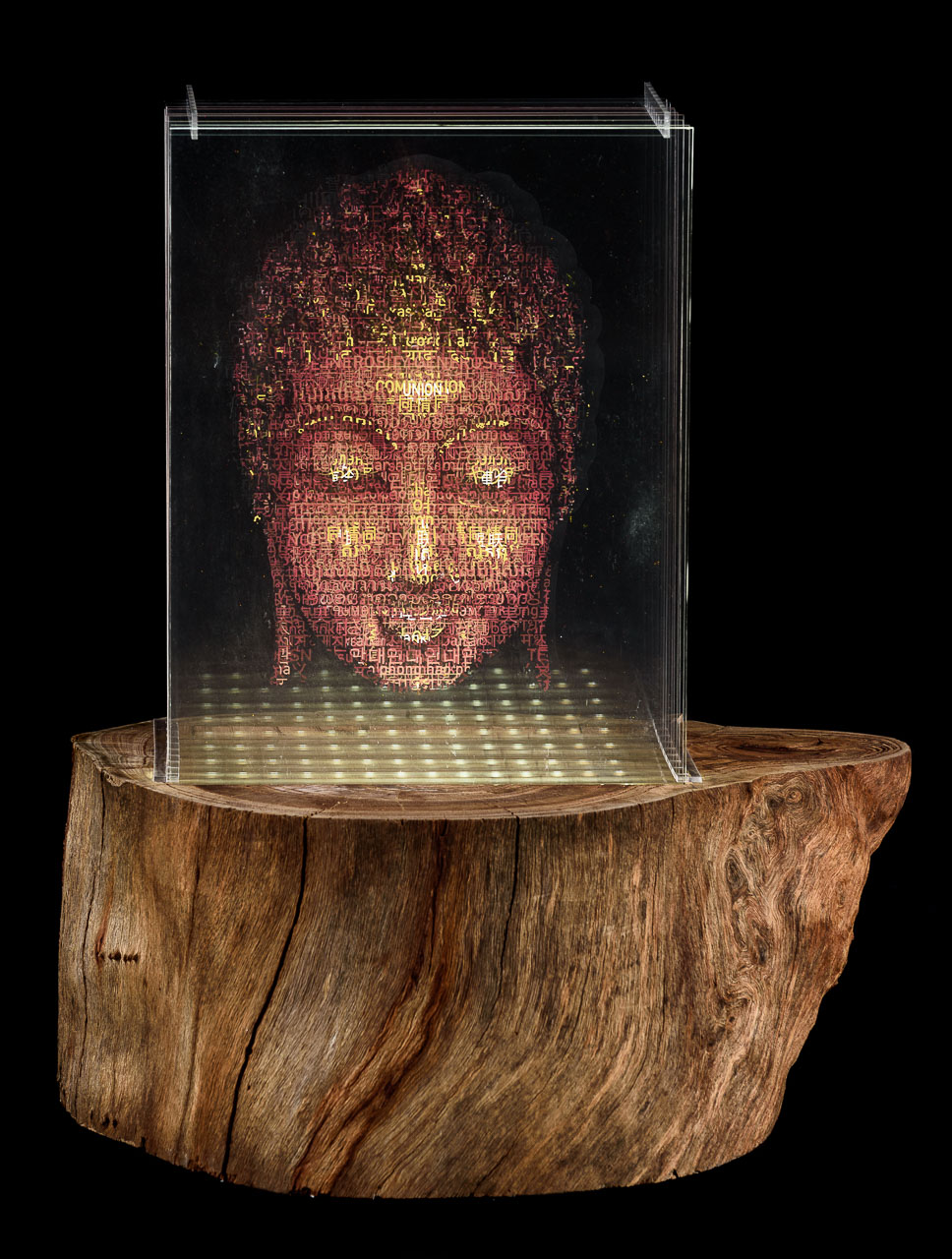 An image of Buddha made of eight layered perspex sheets sitting on top of a segment of tree trunk.
