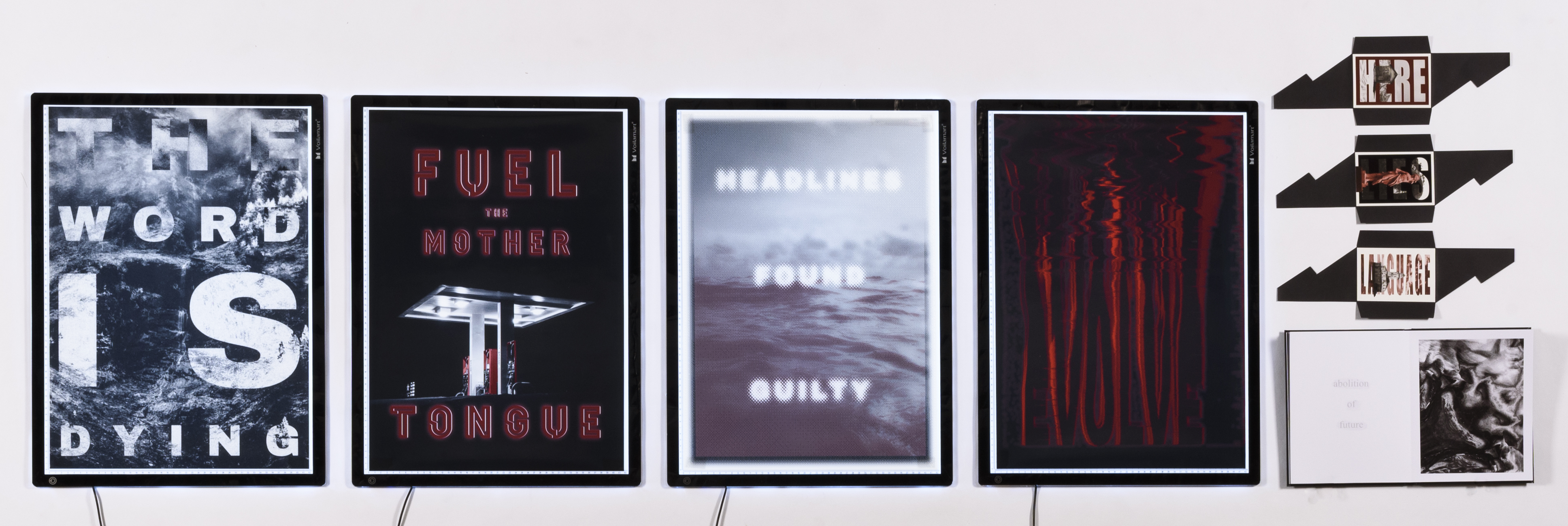 Four light boxes showing text based graphic design works accompanied by four smaller works on paper.