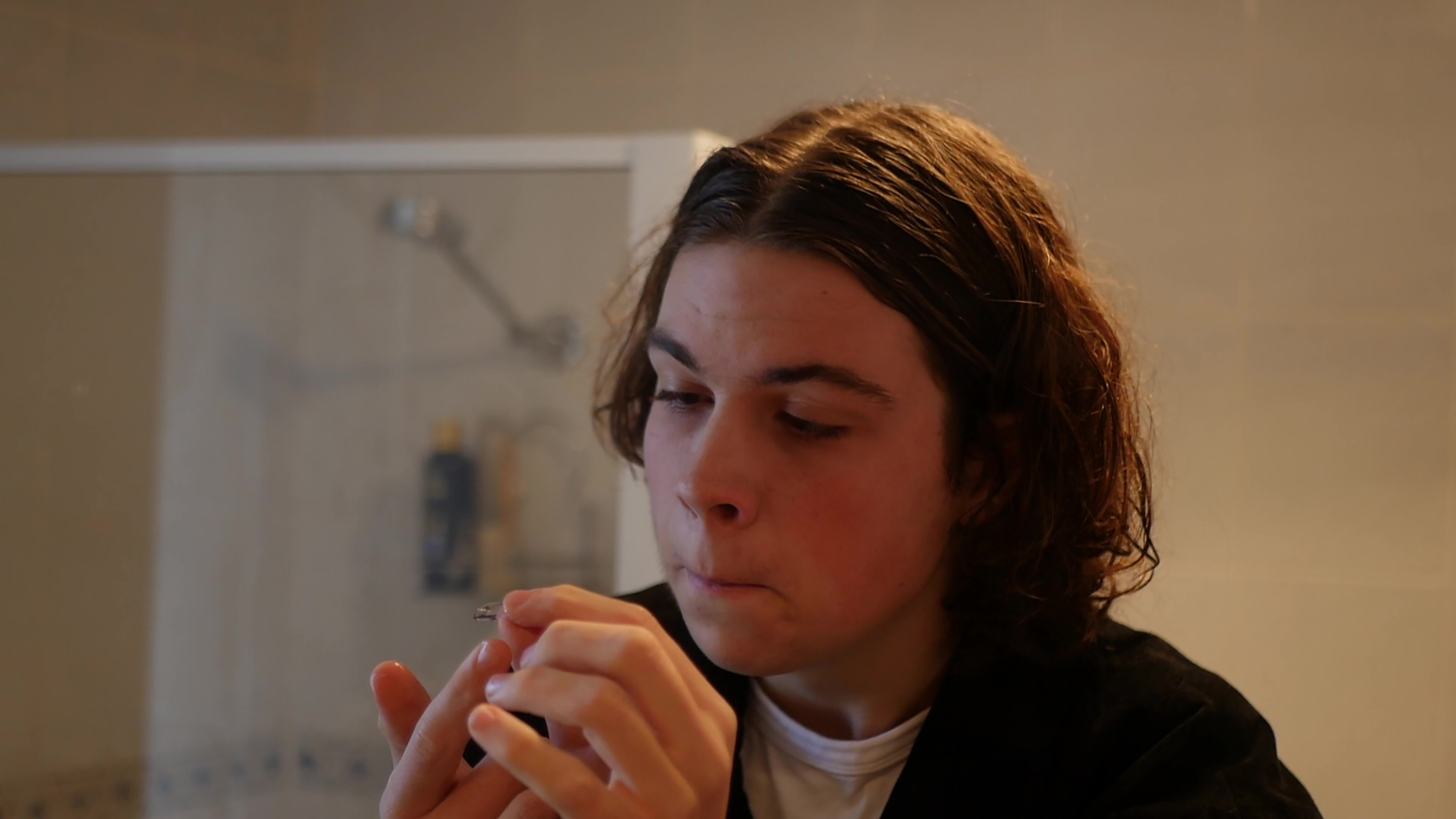 A film still showing a teenage boy with shoulder length hair looking pensive.
