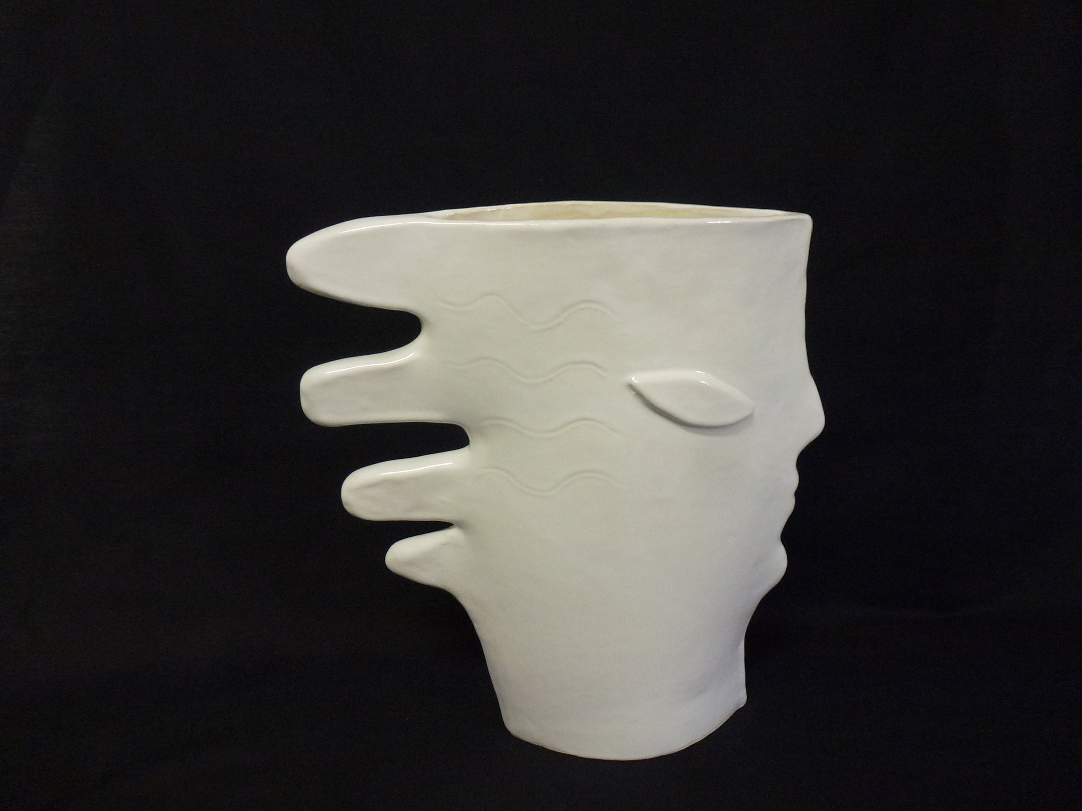 An organic shaped white ceramic vessel photographed on a black background.