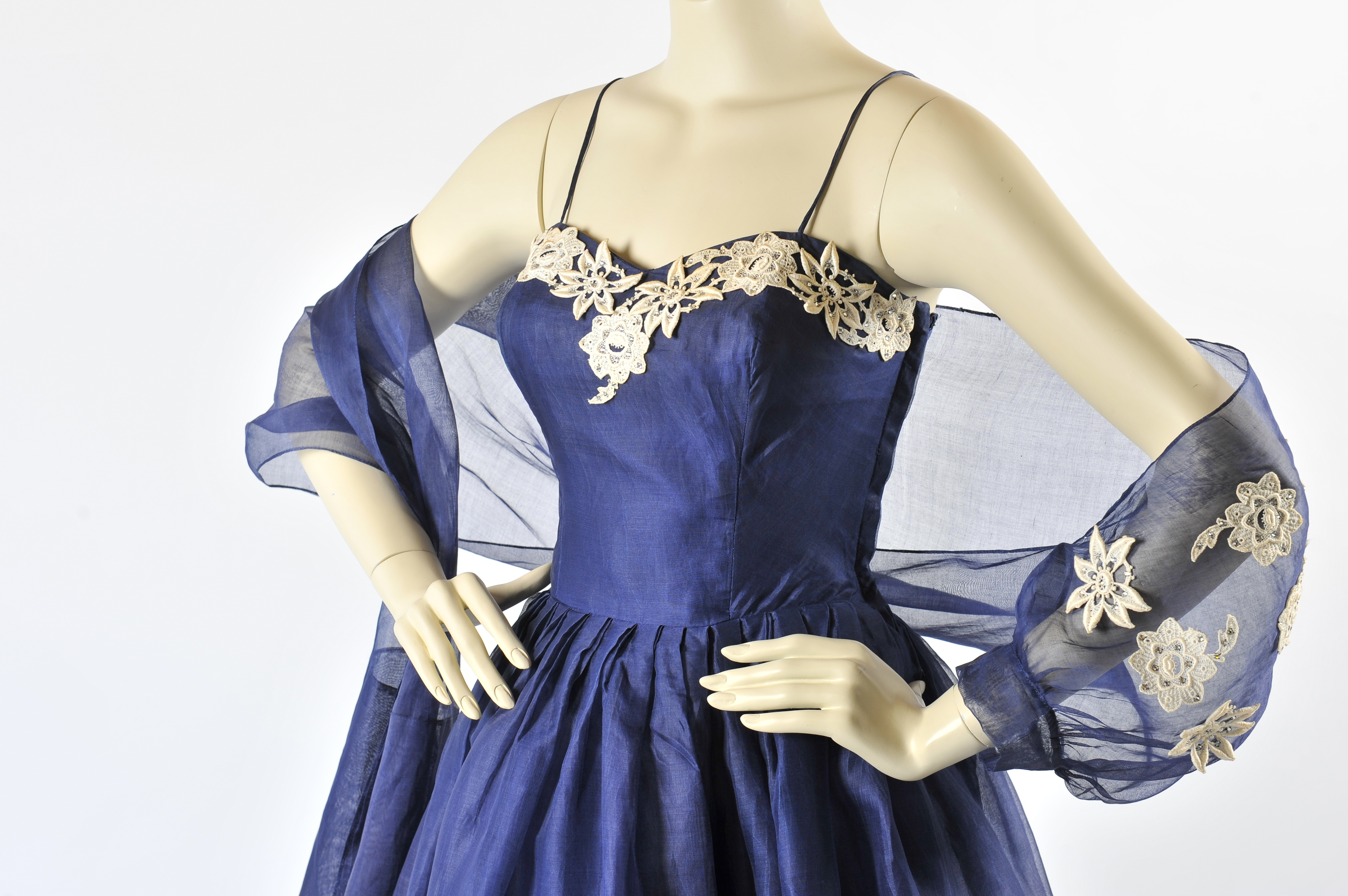 A vintage dress with a sweetheart neckline and spaghetti straps. The dress is a rich blue colour and has white lace applique flowers along the bustline. There is also a sheer matching bolero.