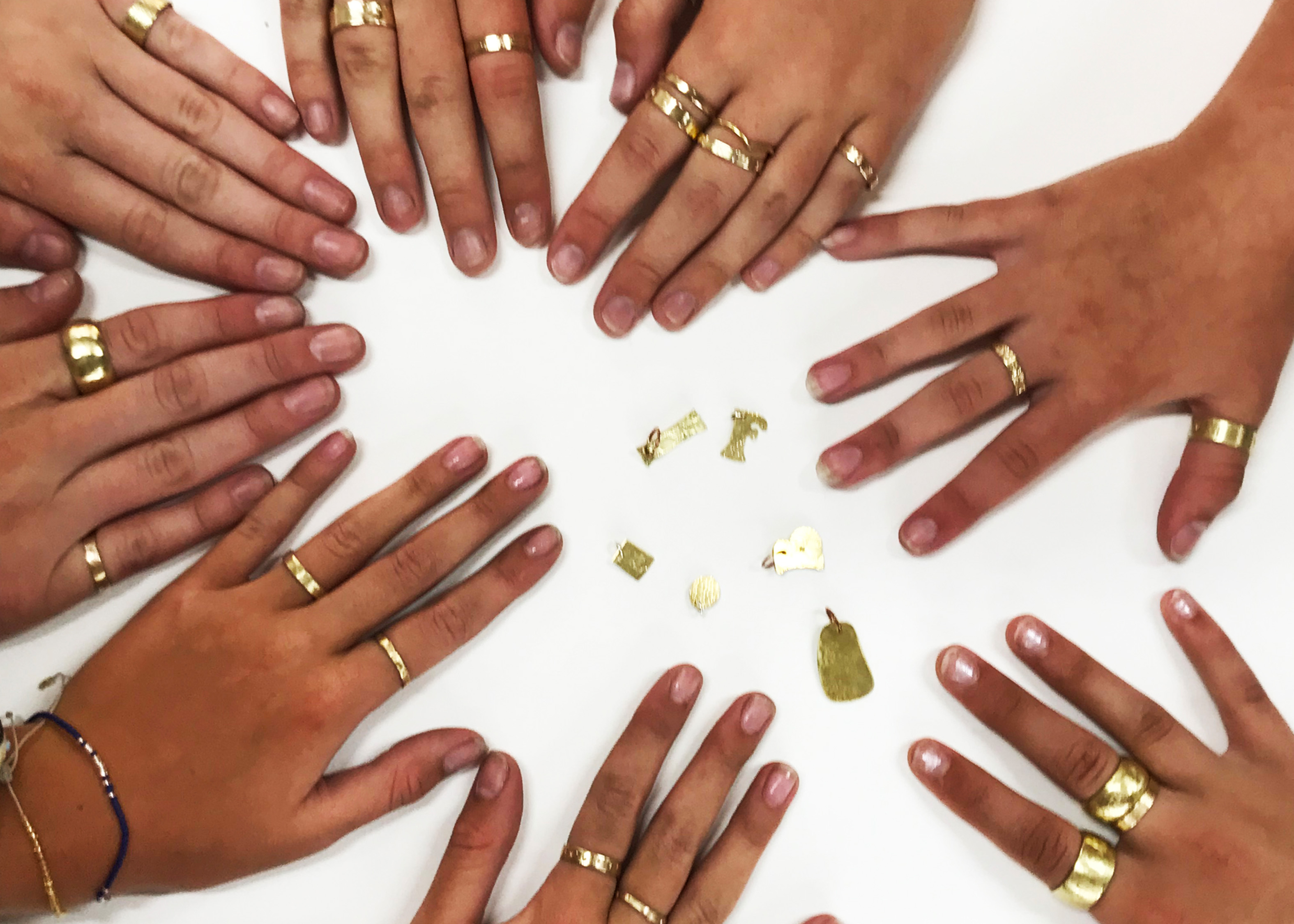 A circle of hangs all wearing rings made from brass.